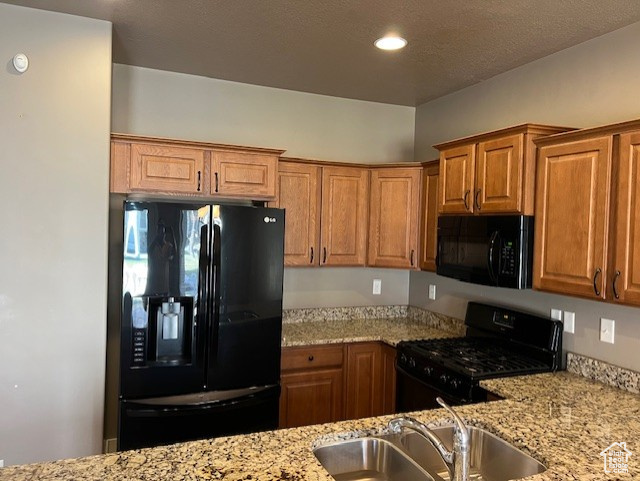 Kitchen featuring black appliances, light stone countertops, brown cabinetry, and recessed lighting