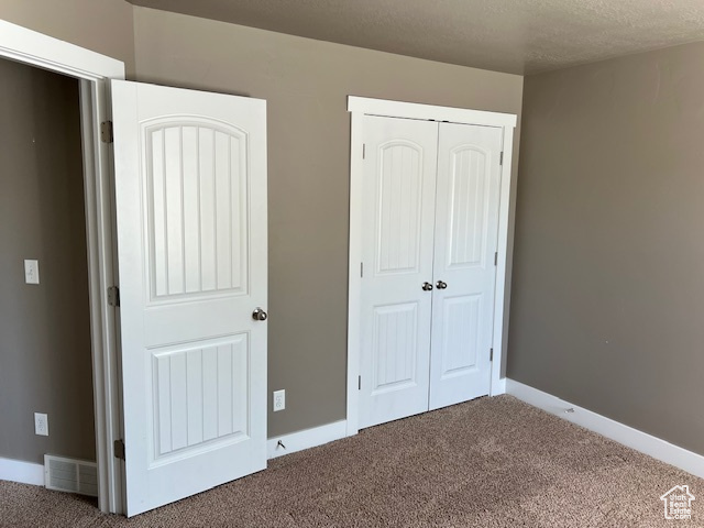 Unfurnished bedroom with carpet, a closet, and a textured ceiling