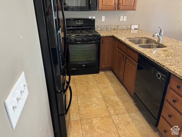 Kitchen featuring black appliances, brown cabinetry, light stone counters, and light tile patterned floors