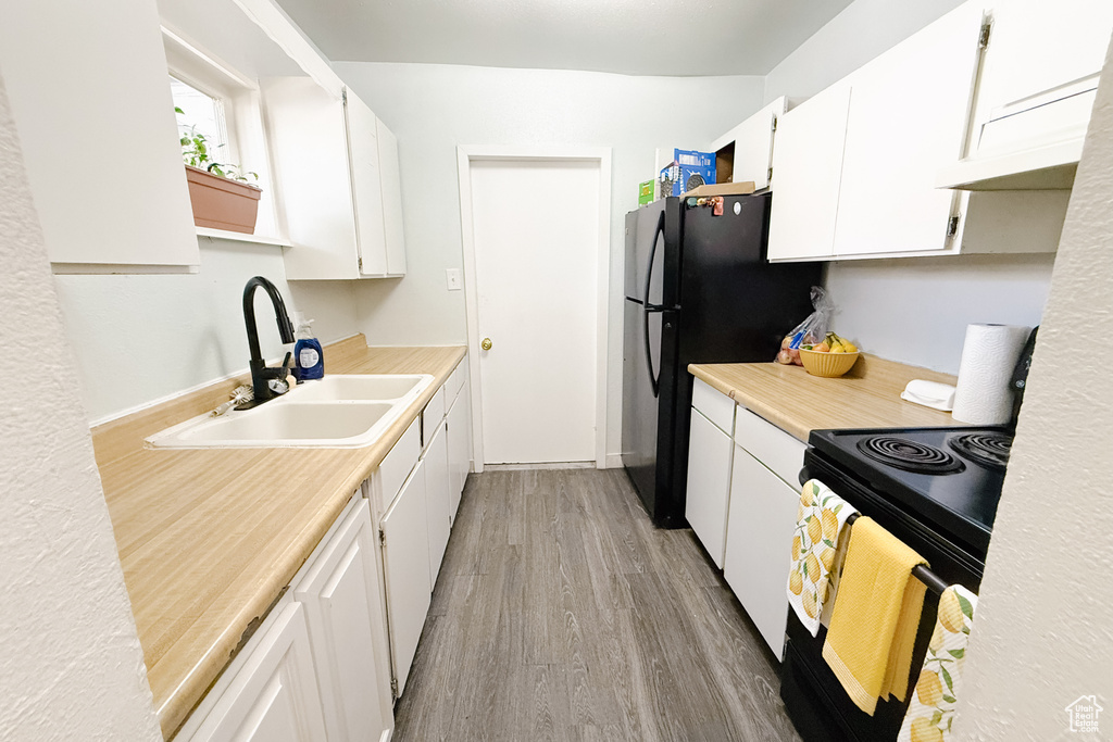 Kitchen with black range with electric cooktop, light wood-style floors, white cabinetry, and light countertops