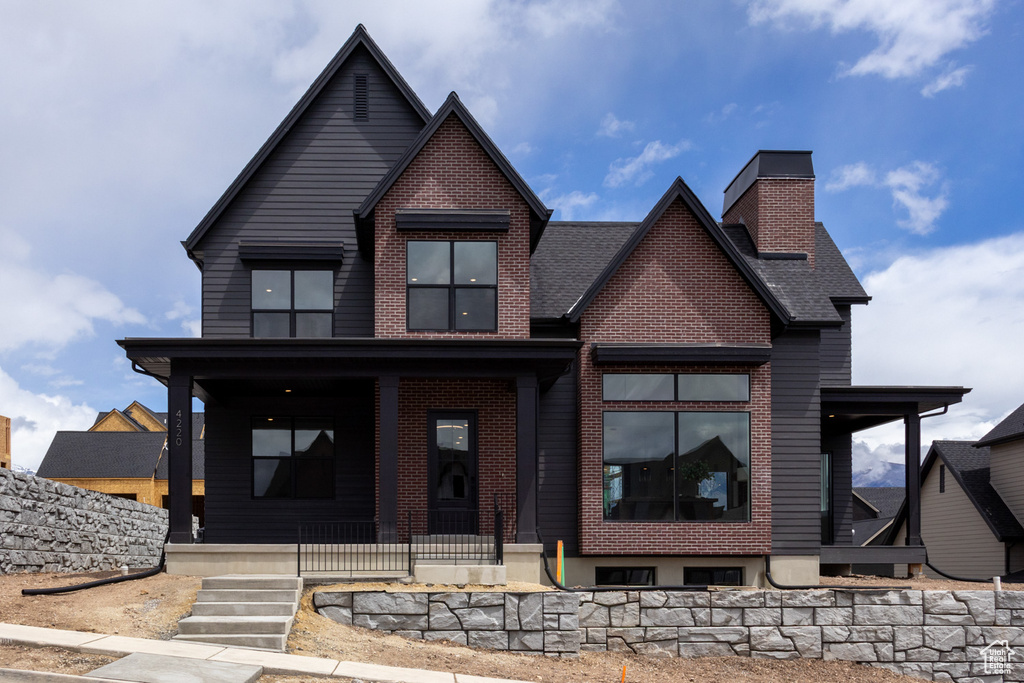 View of front of home with covered porch, a chimney, brick siding, and a shingled roof