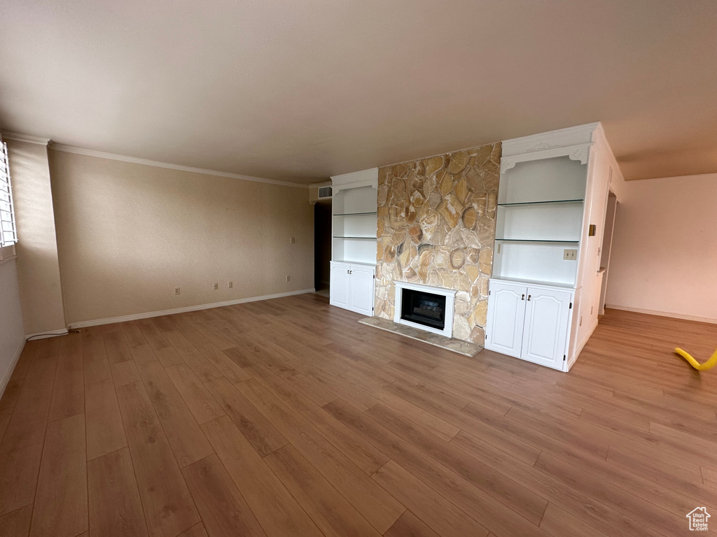 Unfurnished living room with light wood-type flooring, a stone fireplace, built in features, and crown molding