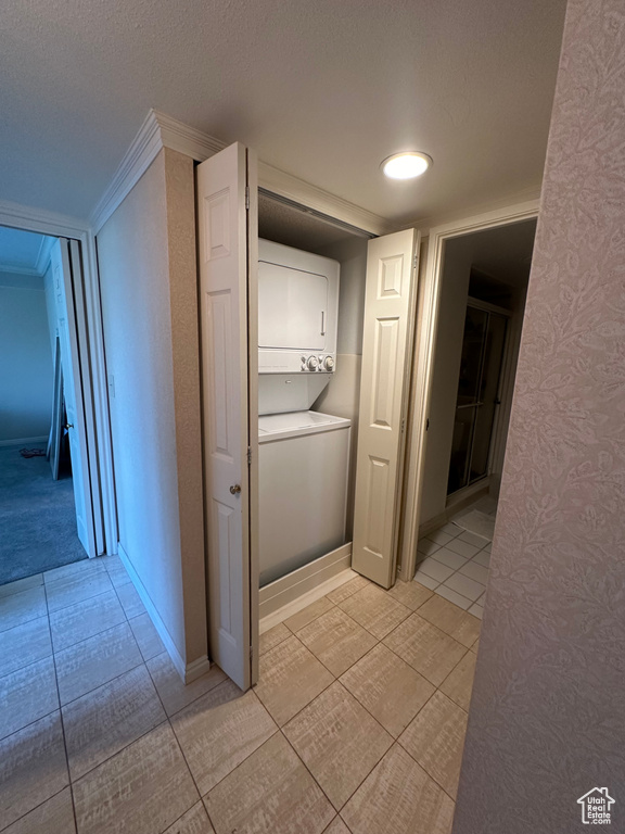 Laundry area with stacked washer / drying machine, light tile patterned floors, wallpapered walls, and crown molding