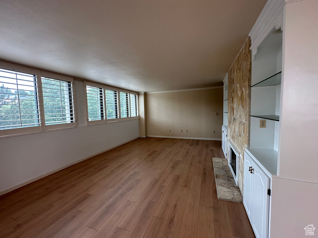 Unfurnished living room with light wood finished floors, ornamental molding, and a fireplace