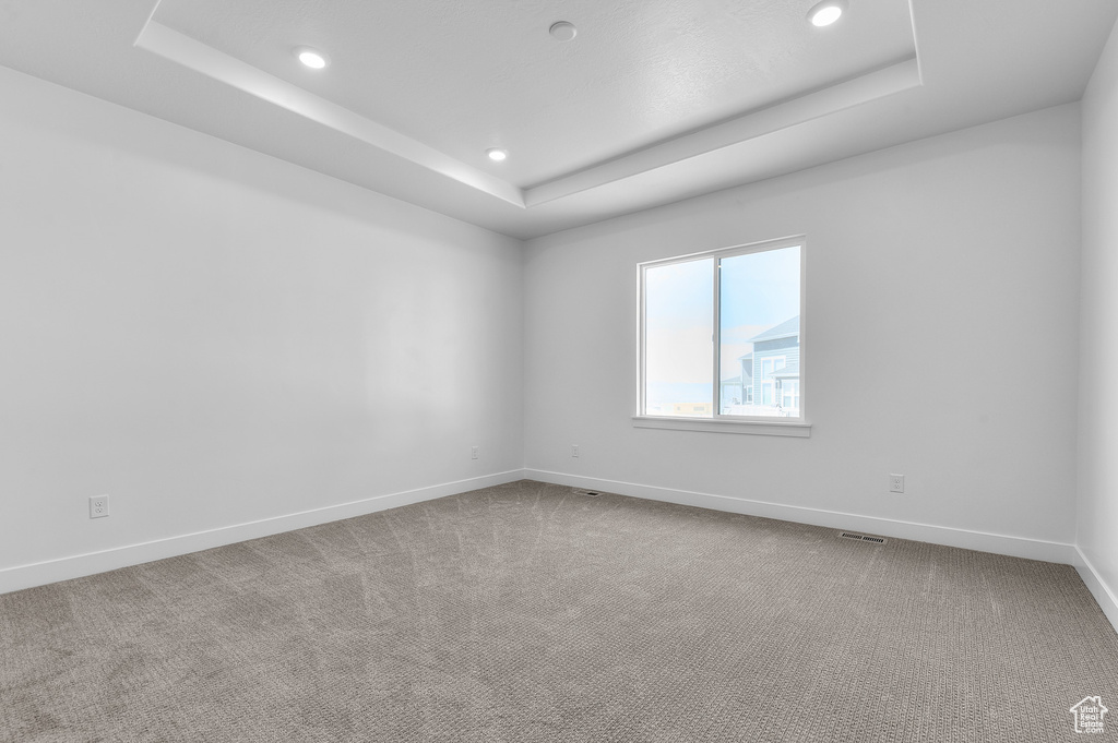 Empty room with a raised ceiling, recessed lighting, and carpet floors
