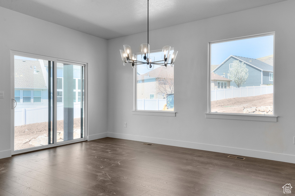 Unfurnished room featuring a chandelier, plenty of natural light, and dark wood-style flooring