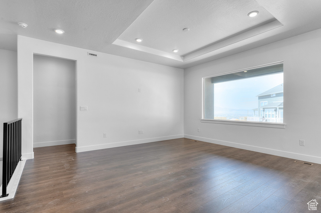 Unfurnished room with a smoke detector, a raised ceiling, dark wood finished floors, recessed lighting, and a textured ceiling