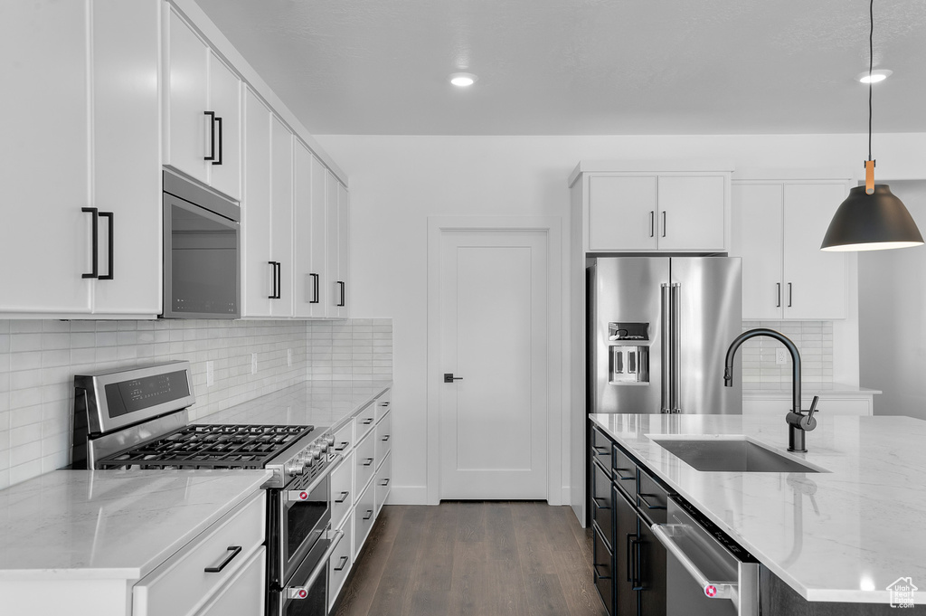 Kitchen with appliances with stainless steel finishes, dark wood-style floors, light stone counters, pendant lighting, and decorative backsplash
