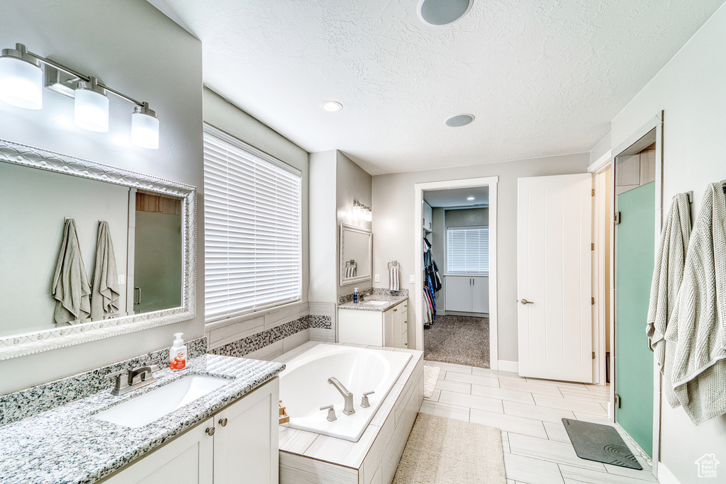 Bathroom featuring two vanities, a bath, a textured ceiling, recessed lighting, and a walk in closet