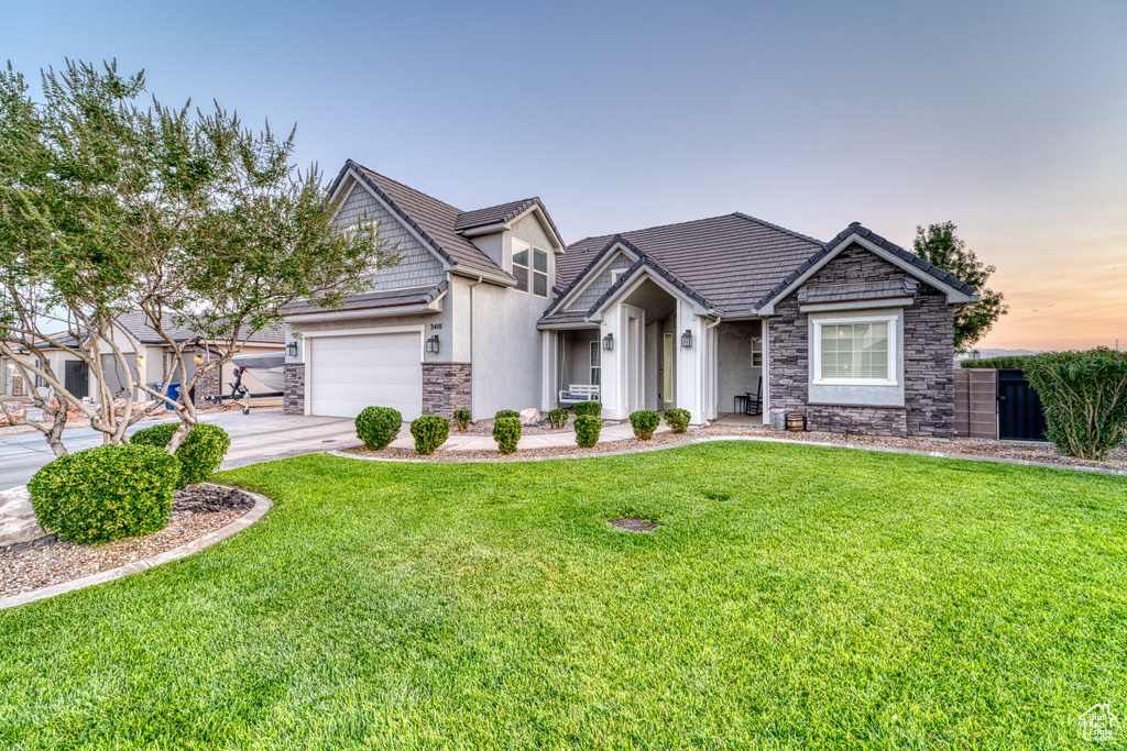 View of front of home with stone siding, stucco siding, a front yard, driveway, and a garage