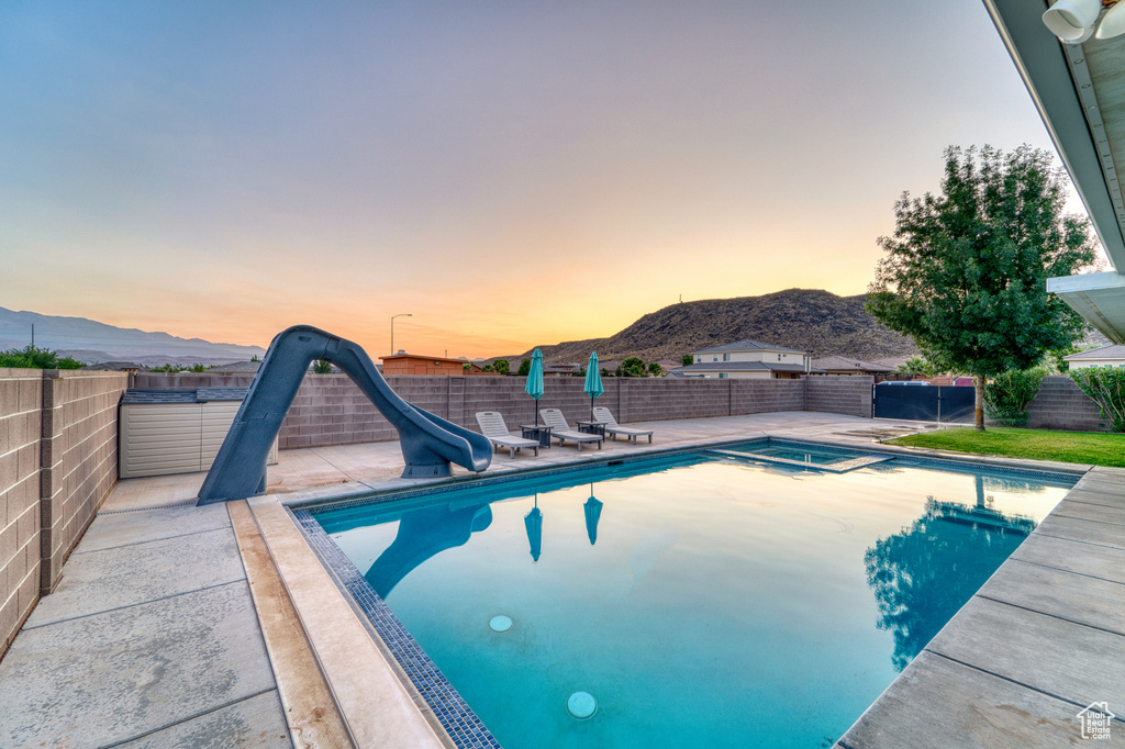 View of pool with a water slide, a mountain view, a fenced backyard, and a patio