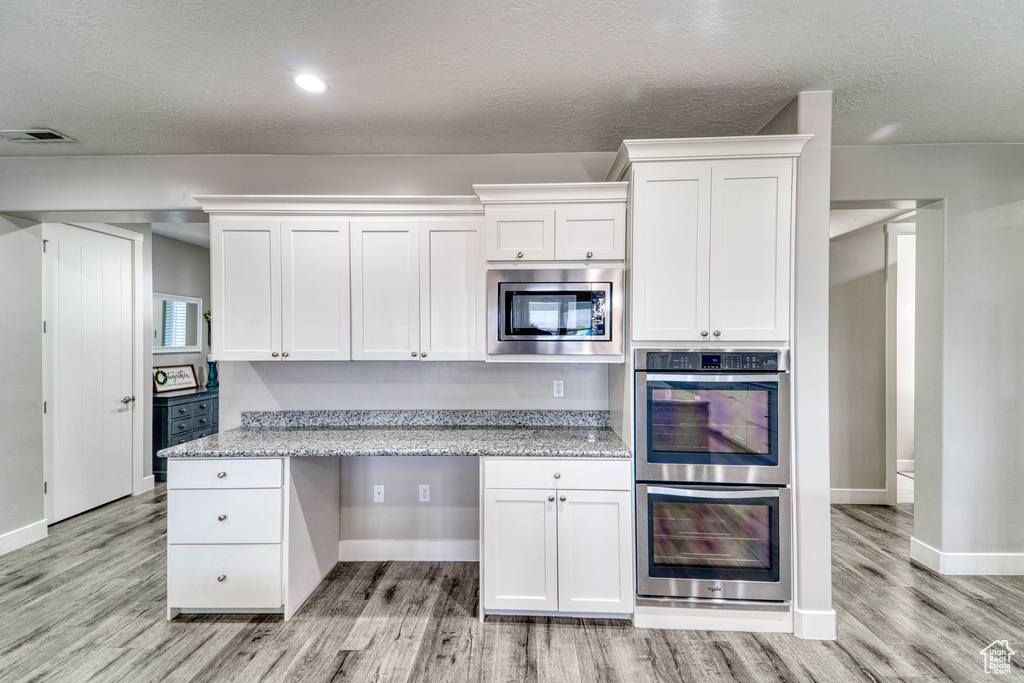 Kitchen with appliances with stainless steel finishes, light wood finished floors, white cabinets, a textured ceiling, and recessed lighting