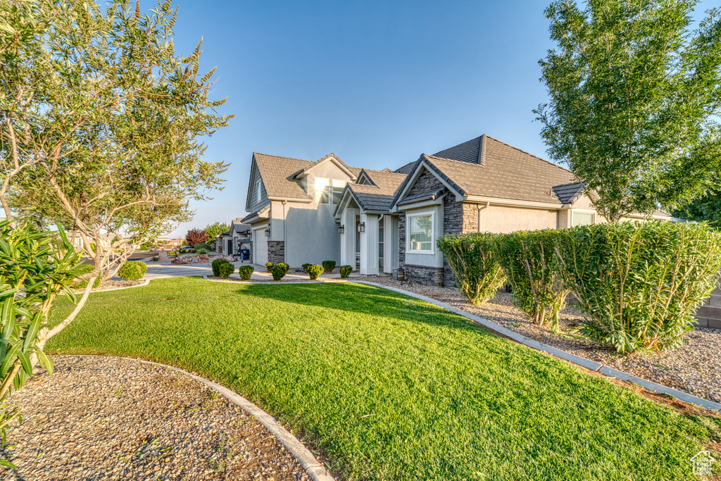 View of front facade featuring stone siding, stucco siding, a front lawn, and roof with shingles