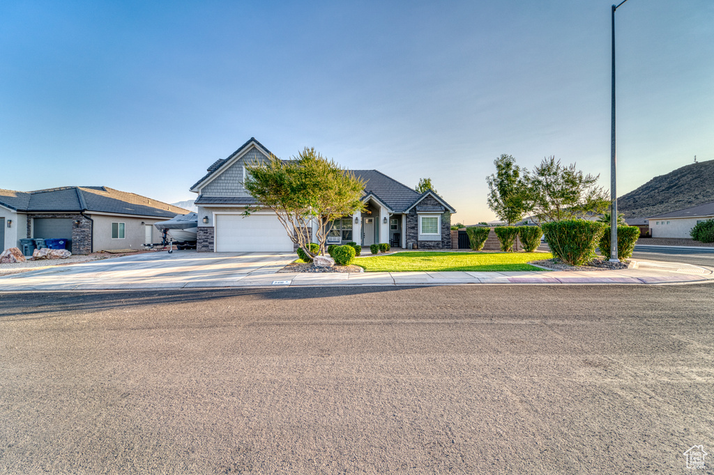 View of front of home with driveway, stone siding, an attached garage, and a front lawn