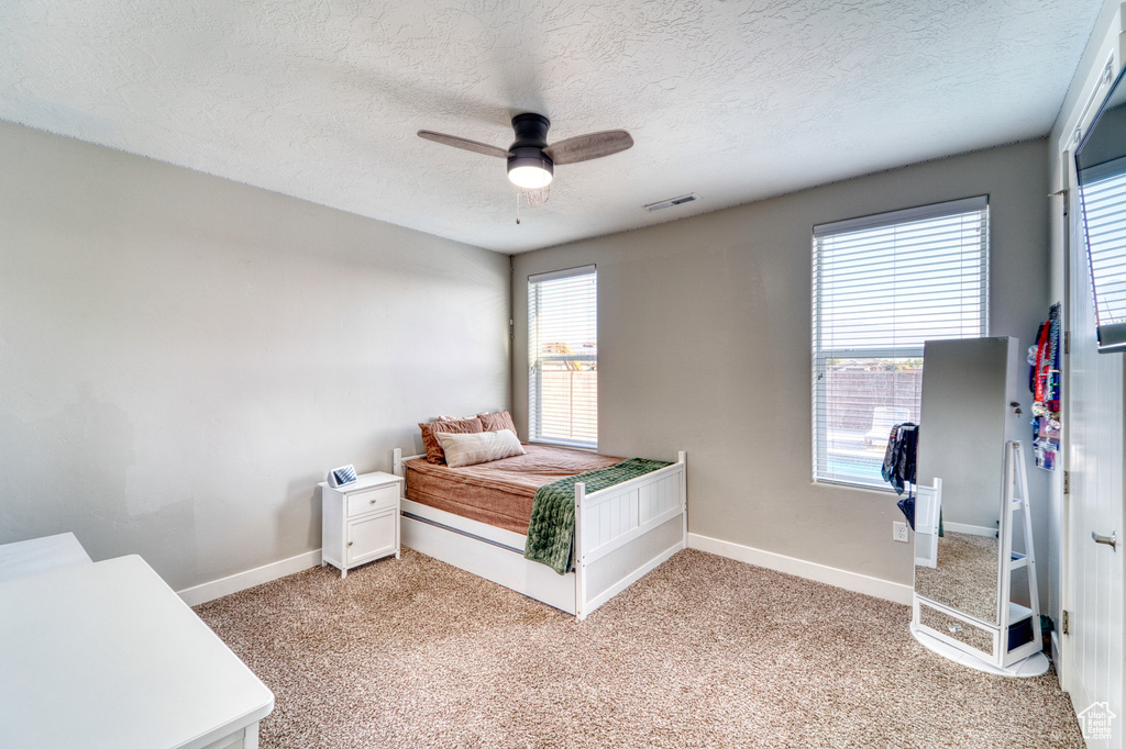 Bedroom with a textured ceiling, light colored carpet, and ceiling fan