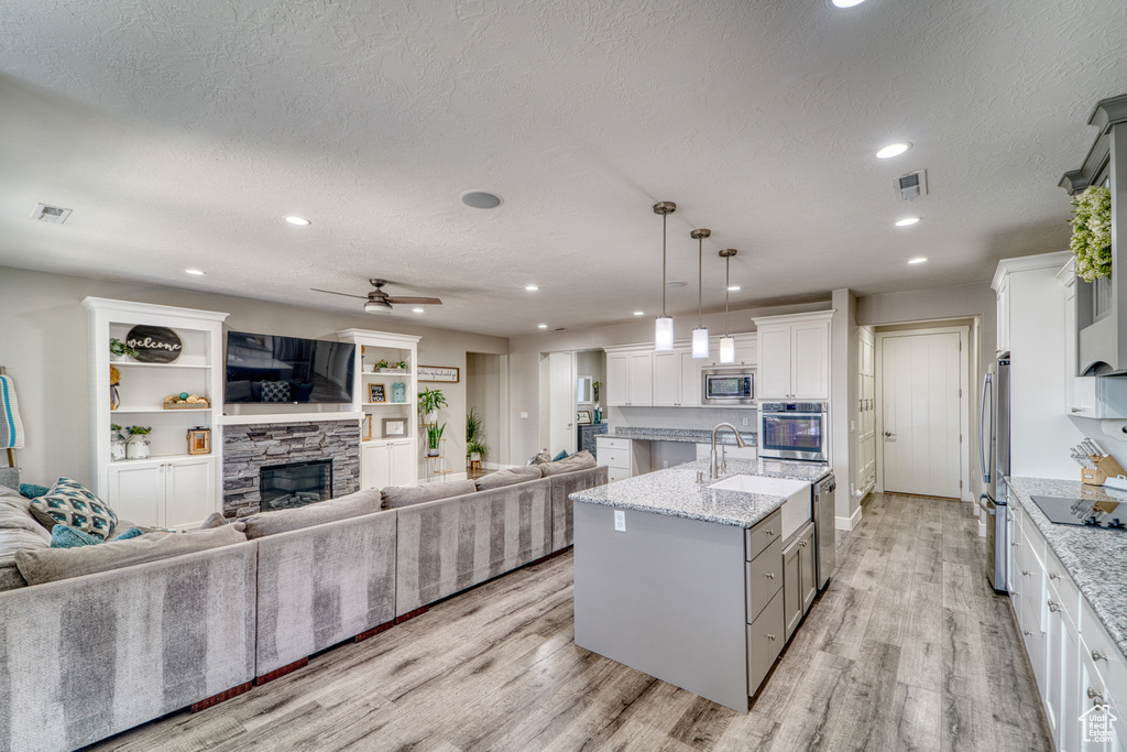 Kitchen with appliances with stainless steel finishes, open floor plan, light wood finished floors, a kitchen island with sink, and a textured ceiling
