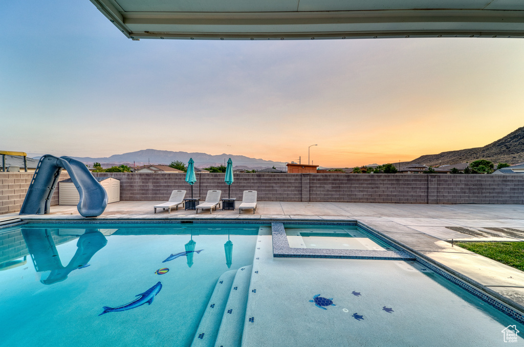Pool at dusk featuring a mountain view, a water slide, a patio, and a pool with connected hot tub