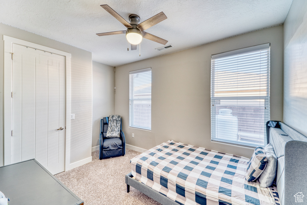 Carpeted bedroom featuring a ceiling fan and a textured ceiling