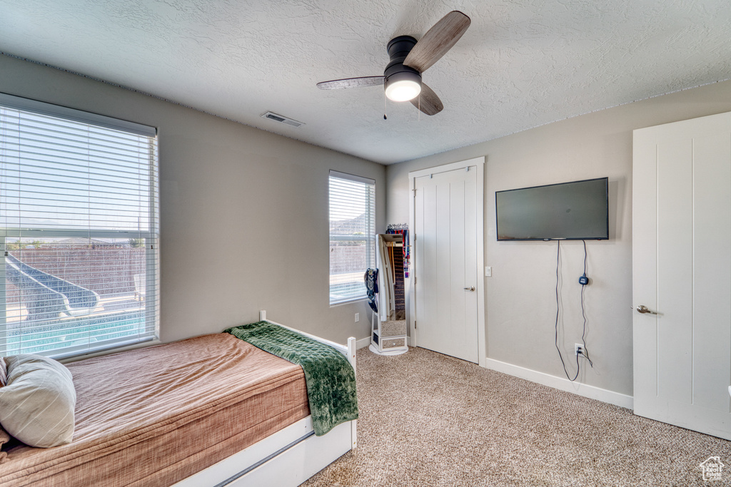 Bedroom with a textured ceiling, light carpet, and a ceiling fan