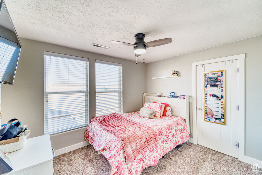 Carpeted bedroom featuring multiple windows, a textured ceiling, and ceiling fan