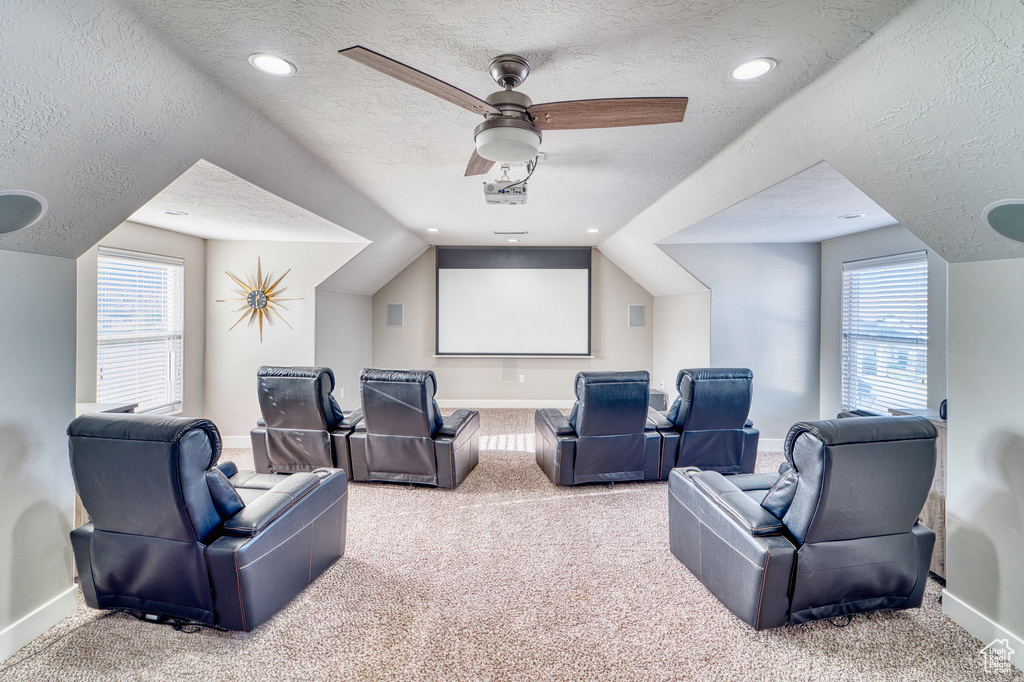 Carpeted home theater with a textured ceiling, ceiling fan, healthy amount of natural light, and vaulted ceiling