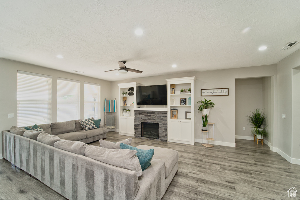 Living room featuring wood finished floors, recessed lighting, a ceiling fan, and a stone fireplace
