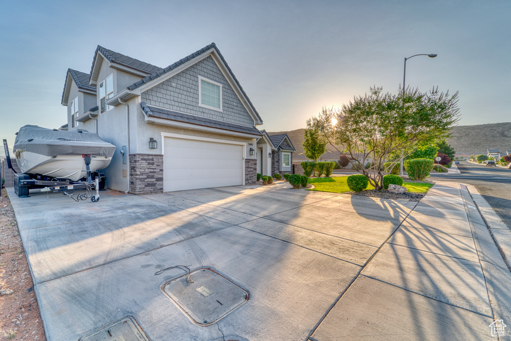 Property exterior at dusk featuring stone siding, concrete driveway, a garage, and stucco siding