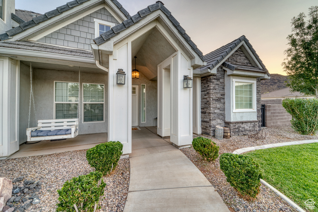View of exterior entry featuring a porch, stone siding, and stucco siding