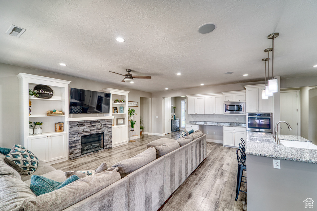 Living room featuring light wood finished floors, recessed lighting, a fireplace, a textured ceiling, and a ceiling fan