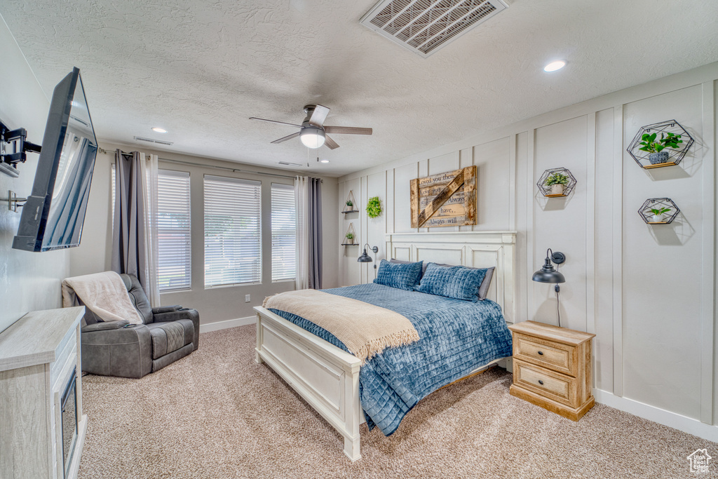 Bedroom featuring light carpet, a decorative wall, a textured ceiling, recessed lighting, and a ceiling fan