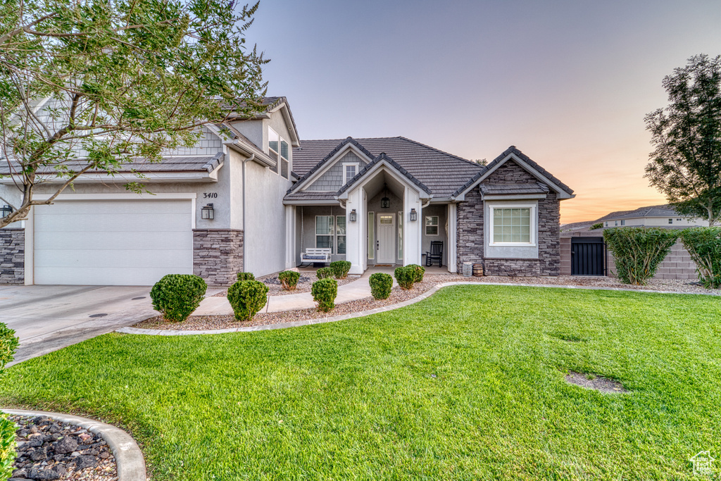 View of front of house featuring stone siding, a front yard, concrete driveway, a garage, and a tile roof