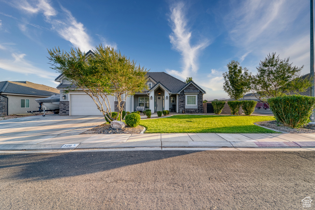 View of front of house with stone siding, concrete driveway, an attached garage, and a front lawn