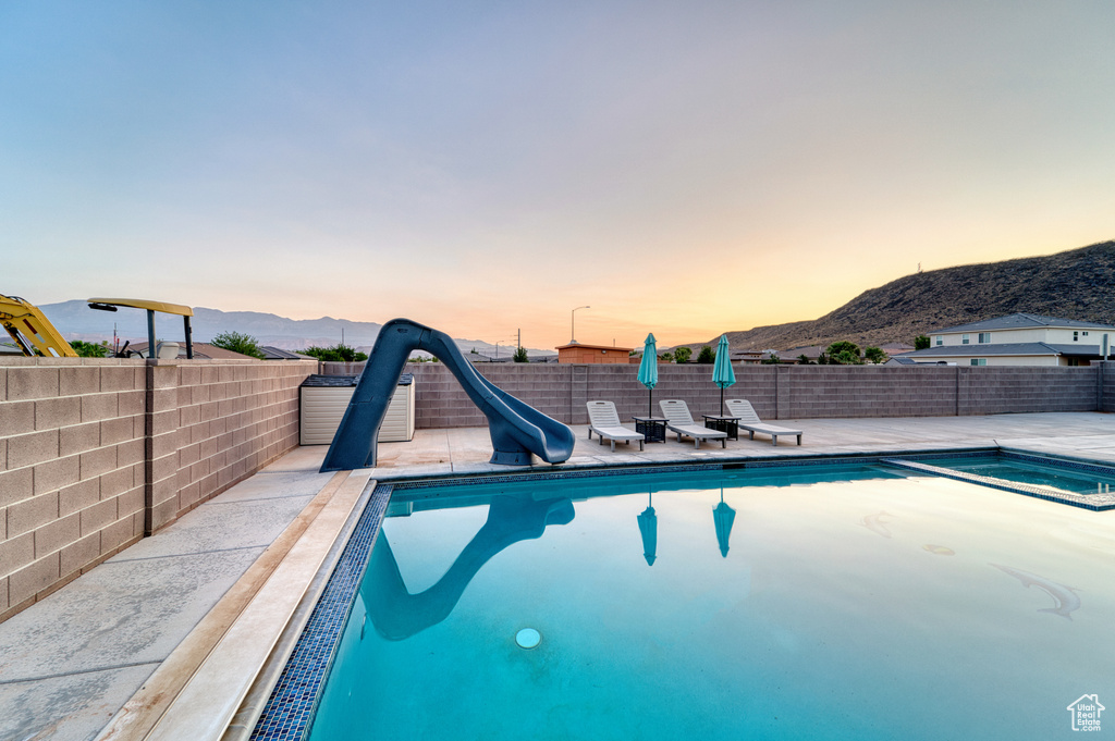 Pool at dusk with a mountain view, a water slide, and a patio