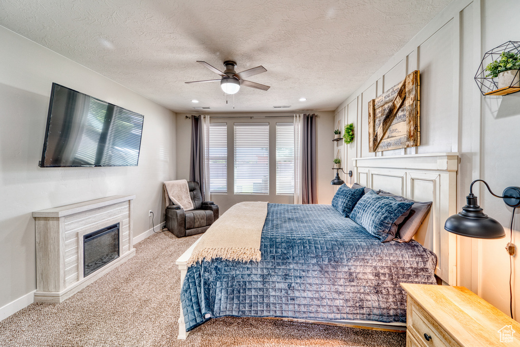 Bedroom with a glass covered fireplace, carpet flooring, a textured ceiling, and ceiling fan