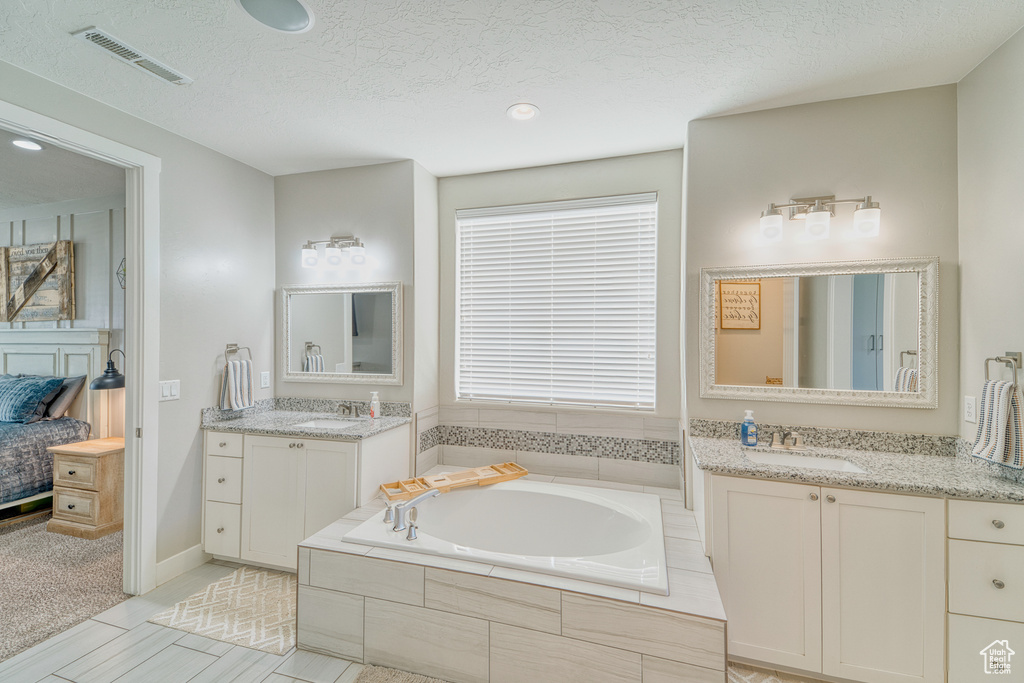 Ensuite bathroom featuring a garden tub, two vanities, a textured ceiling, and recessed lighting