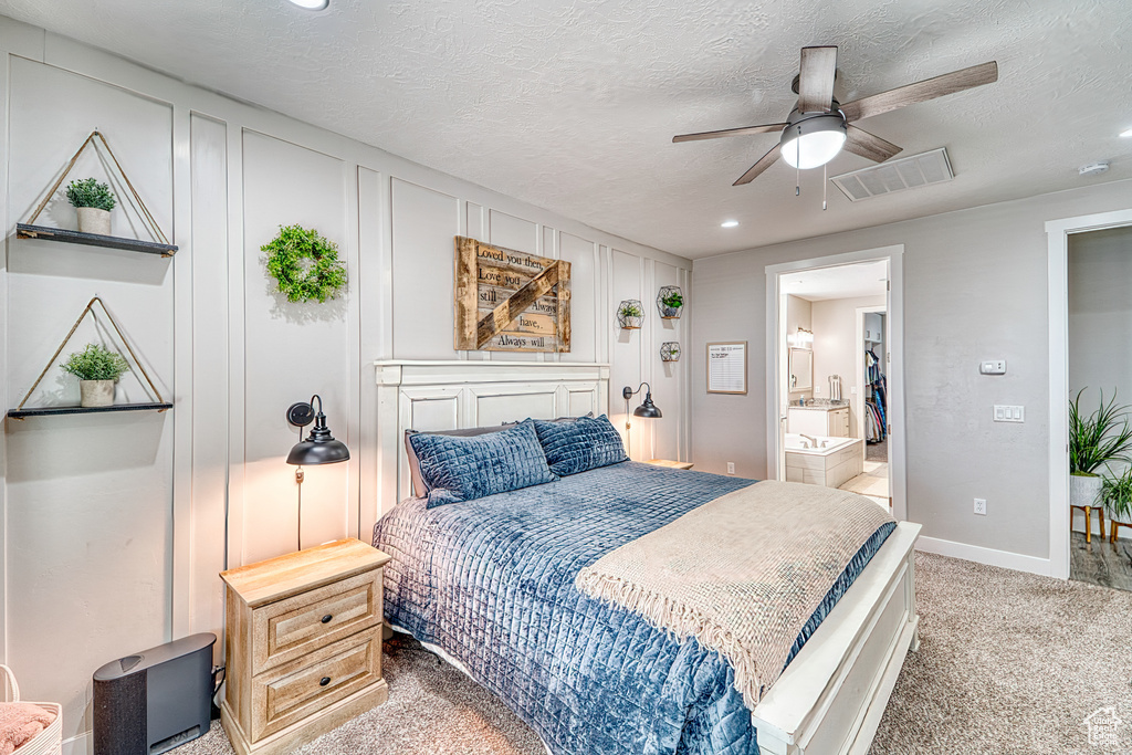 Bedroom with light colored carpet, recessed lighting, a textured ceiling, a decorative wall, and ensuite bathroom