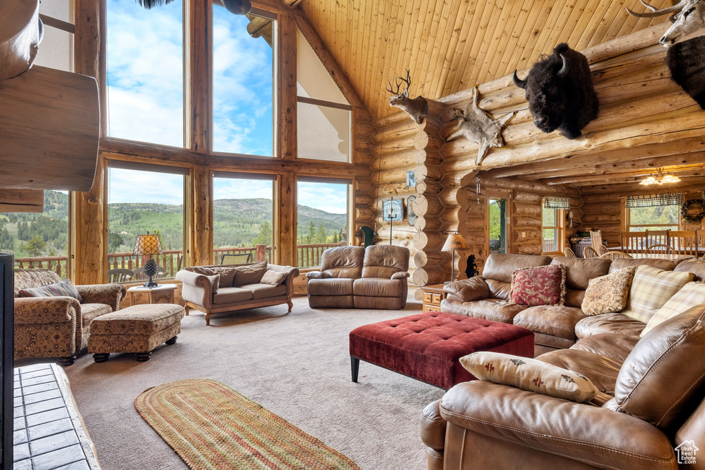 Carpeted living area with high vaulted ceiling, rustic walls, a mountain view, healthy amount of natural light, and wooden ceiling