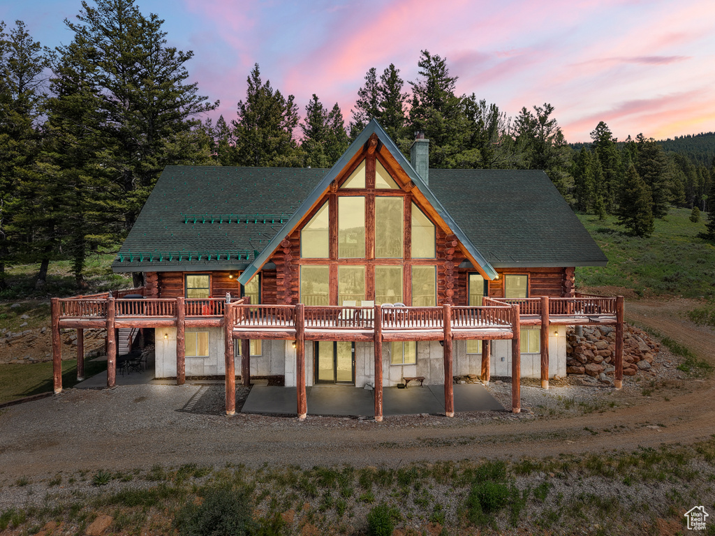Back of property at dusk with log exterior, a deck, a chimney, and a patio