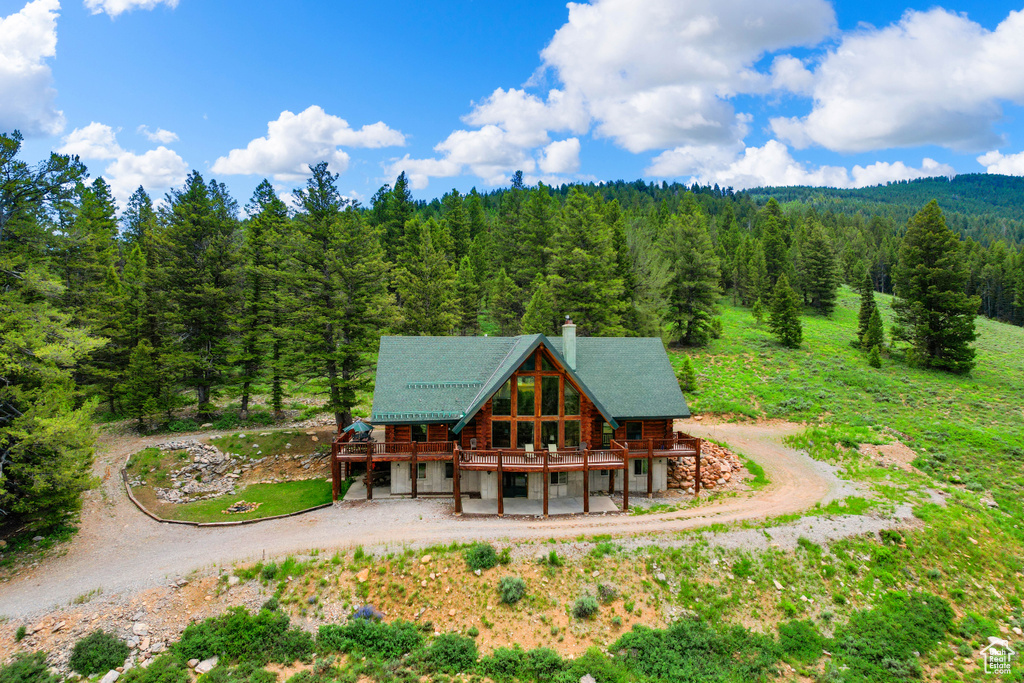 Back of property with log siding, a wooded view, a deck, and driveway