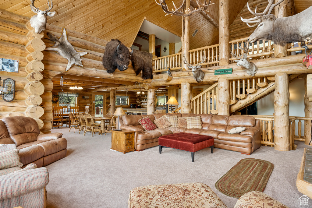 Living area with a towering ceiling, log walls, carpet, a chandelier, and wooden ceiling