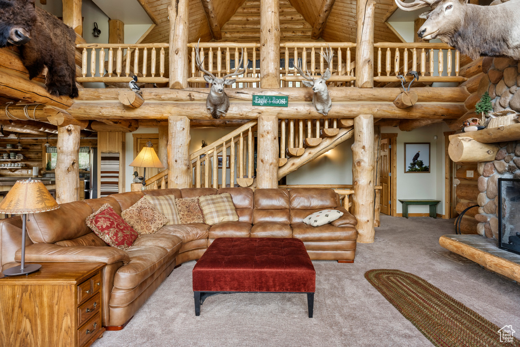 Carpeted living room featuring rustic walls, high vaulted ceiling, a wooden ceiling with exposed beams, and a stone fireplace