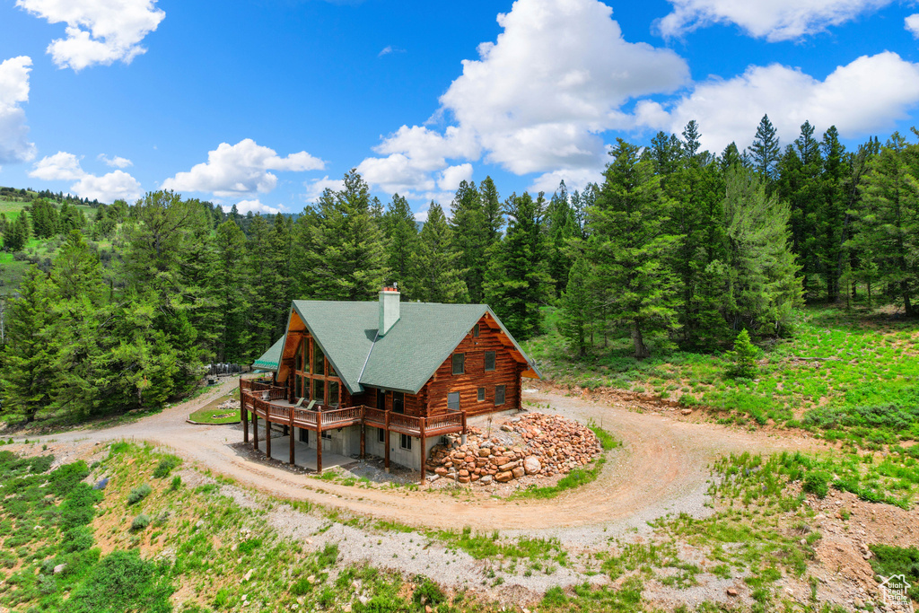 Rear view of property featuring dirt driveway, log exterior, a view of trees, and a chimney