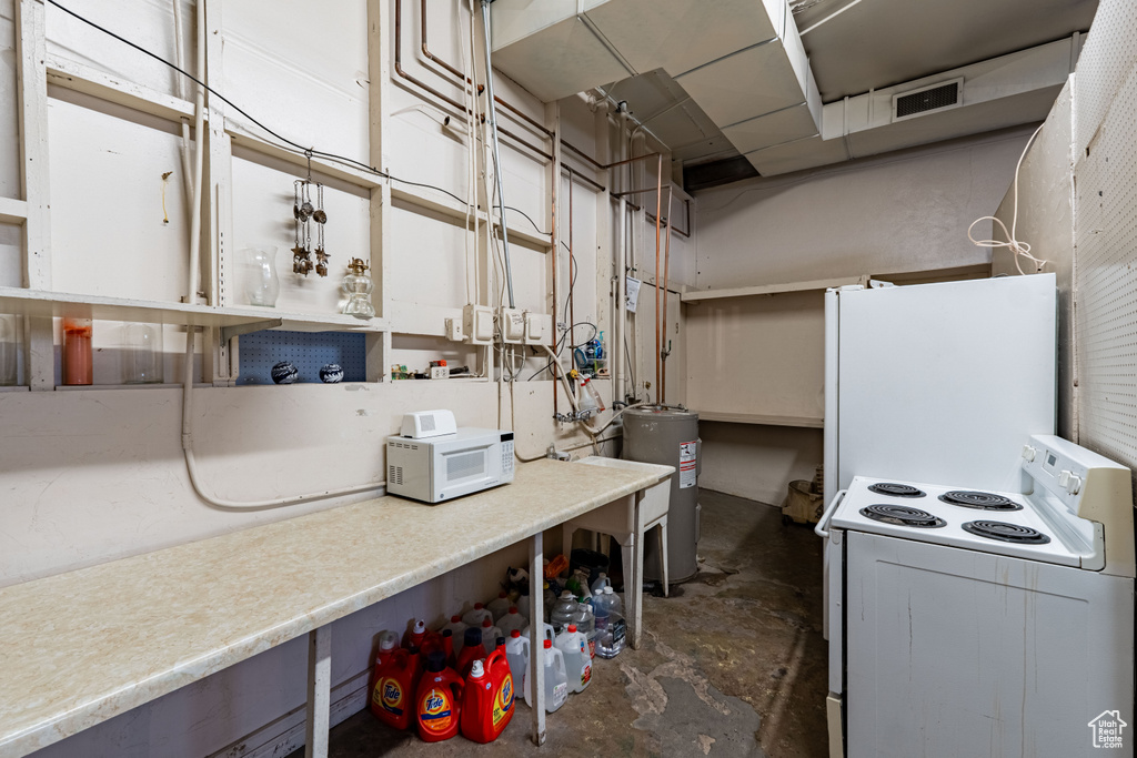 Kitchen featuring white appliances, unfinished concrete flooring, and water heater