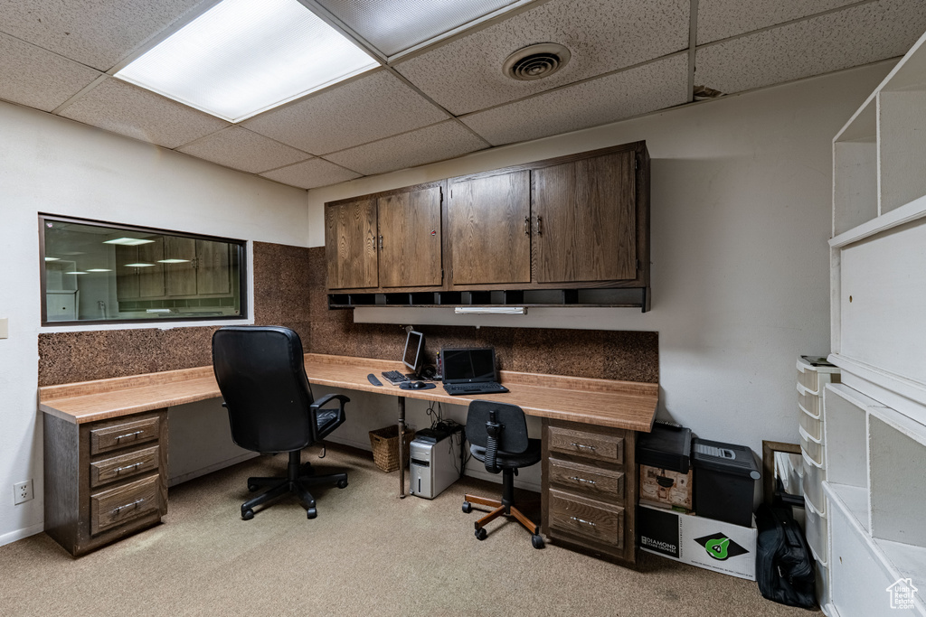 Office space with a paneled ceiling, light carpet, and built in desk