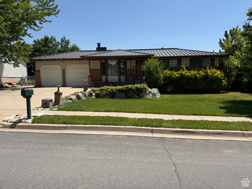 Single story home featuring an attached garage, concrete driveway, a chimney, a front yard, and a standing seam roof