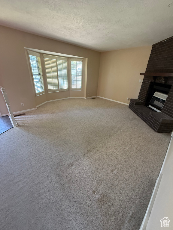 Unfurnished living room with a fireplace, carpet floors, and a textured ceiling