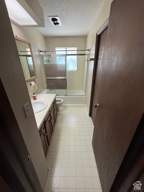 Full bath featuring combined bath / shower with glass door, vanity, and a textured ceiling