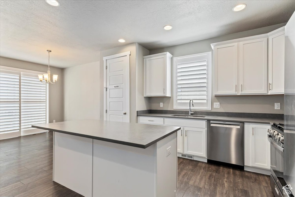 Kitchen with appliances with stainless steel finishes, white cabinets, dark countertops, a chandelier, and dark wood-style flooring
