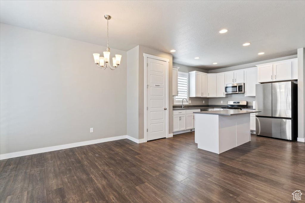 Kitchen with appliances with stainless steel finishes, a chandelier, dark wood-style flooring, white cabinets, and a kitchen island