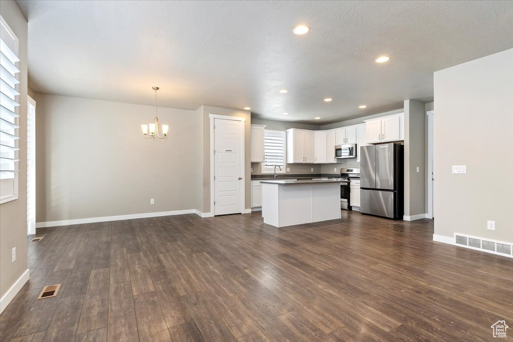 Kitchen with stainless steel appliances, a chandelier, dark countertops, dark wood finished floors, and open floor plan